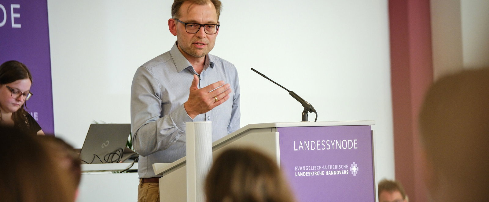 Eine männlich lesbare Person an einem Rednerpult