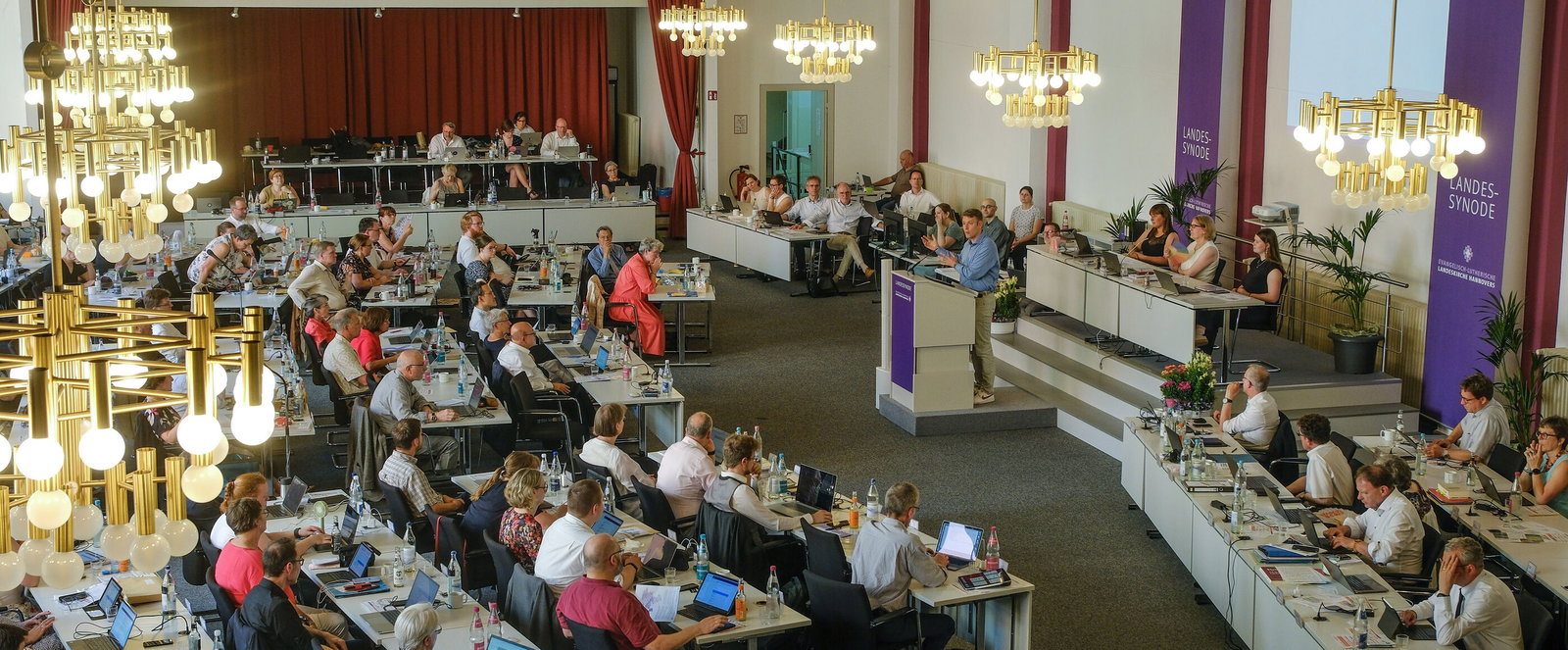 Viele Personen an Tischen in einem Sitzungssaal