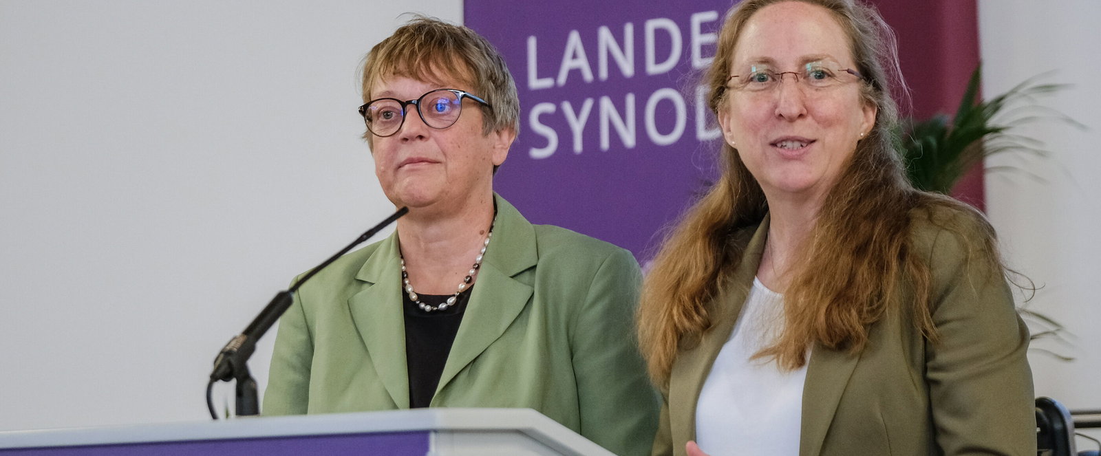 Zwei weiblich lesbare Personen an einem Rednerpult