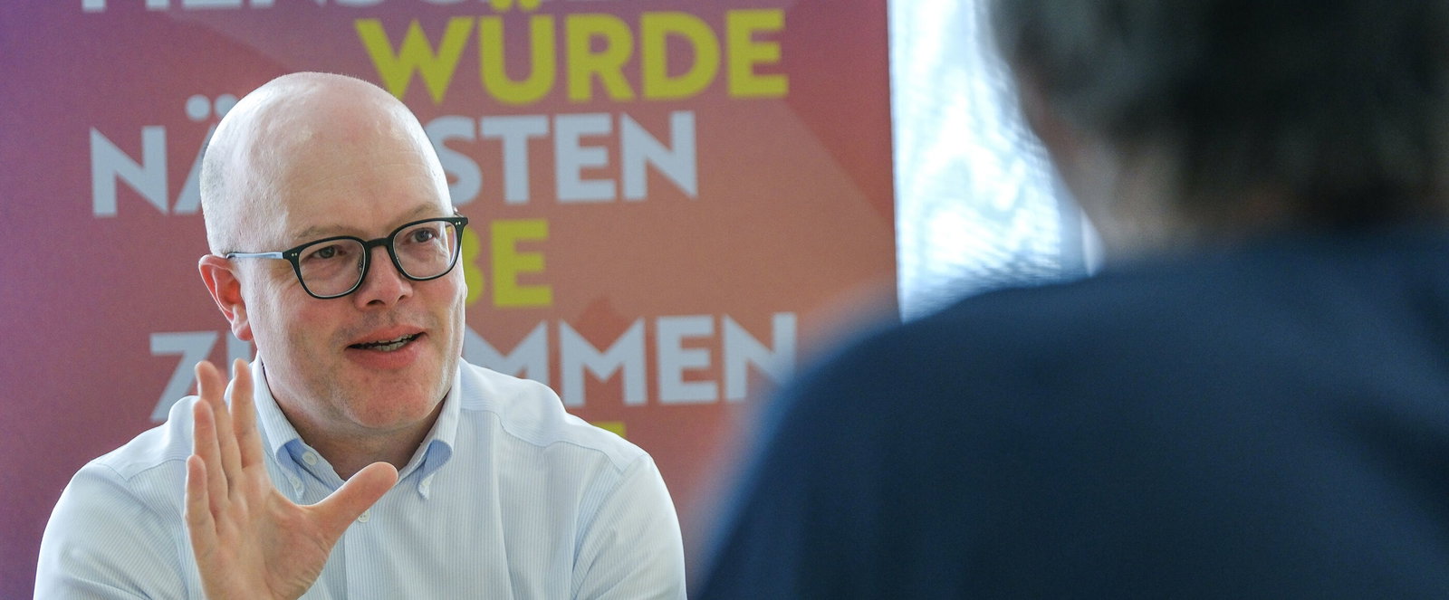 Eine männlich lesbare Person vor einem Roll-up