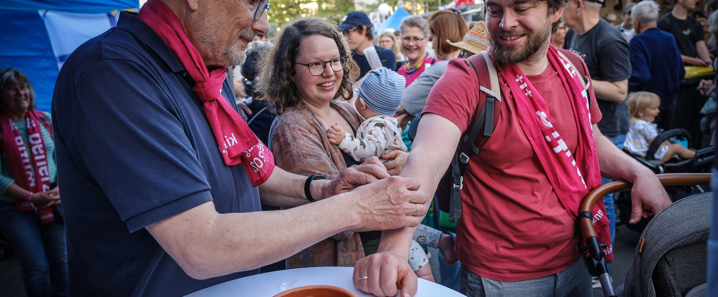 Drei Menschen stehen an einem Stehtisch in mitten einer dicht gedrängten Fußgängerzone in einem Fest.