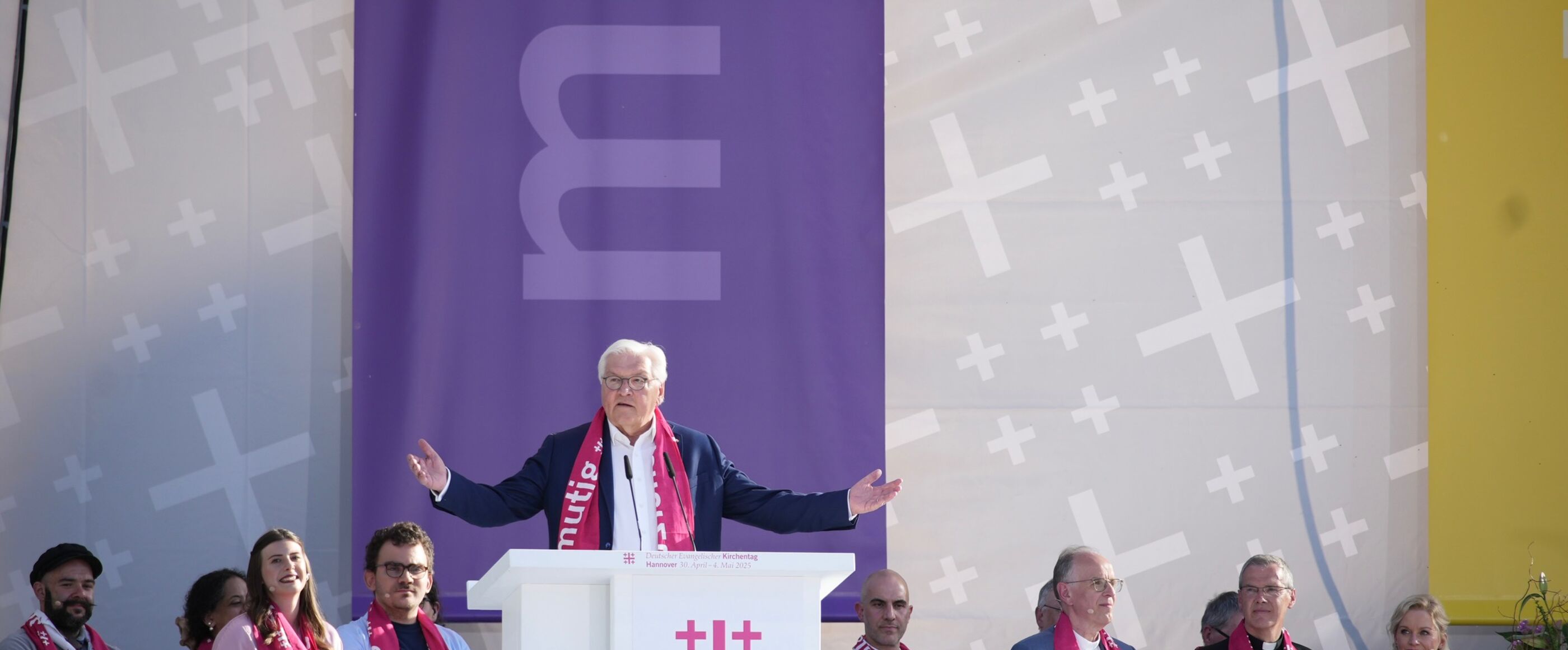ein Mann steht hinter einem Altar, hinter ihm sitzen mehrere Personen