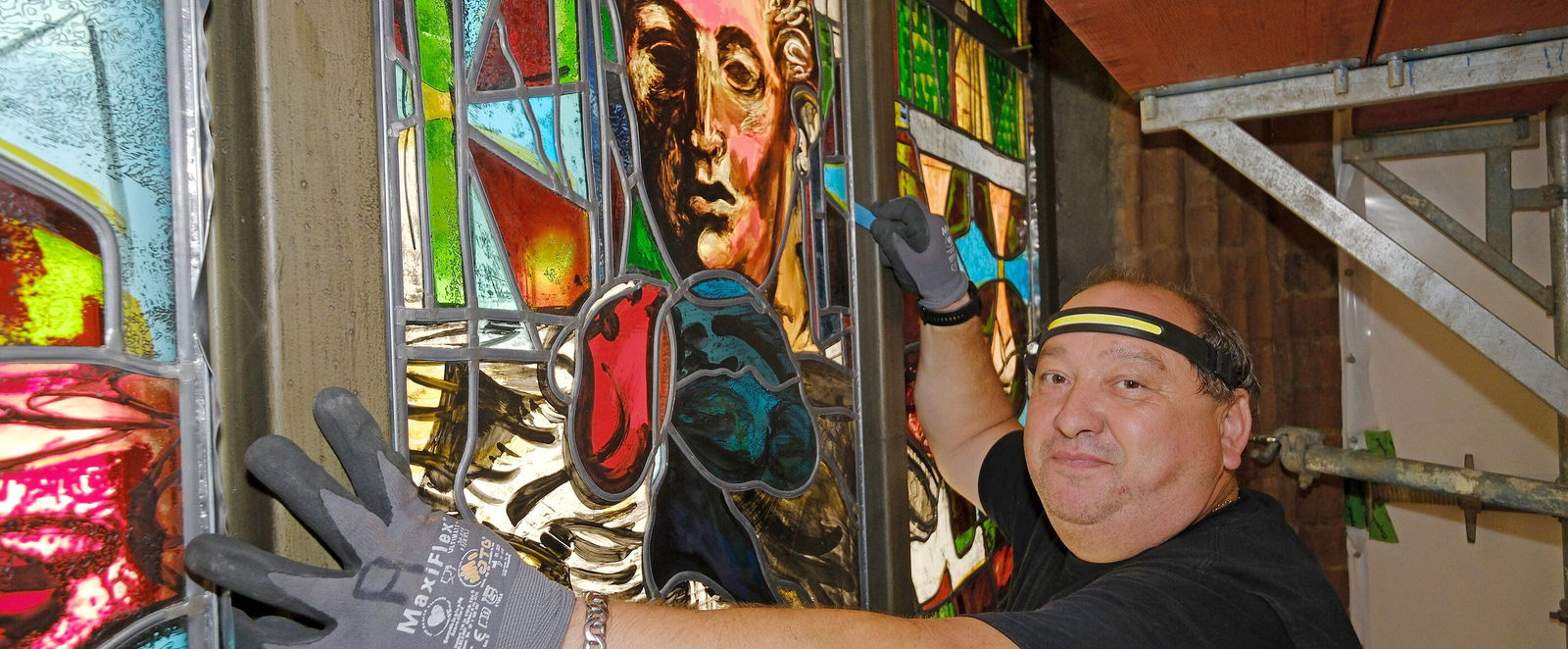 Ein Handwerker mit Kappe und Handschuhen prüft den Sitz eines Kirchenfensters.