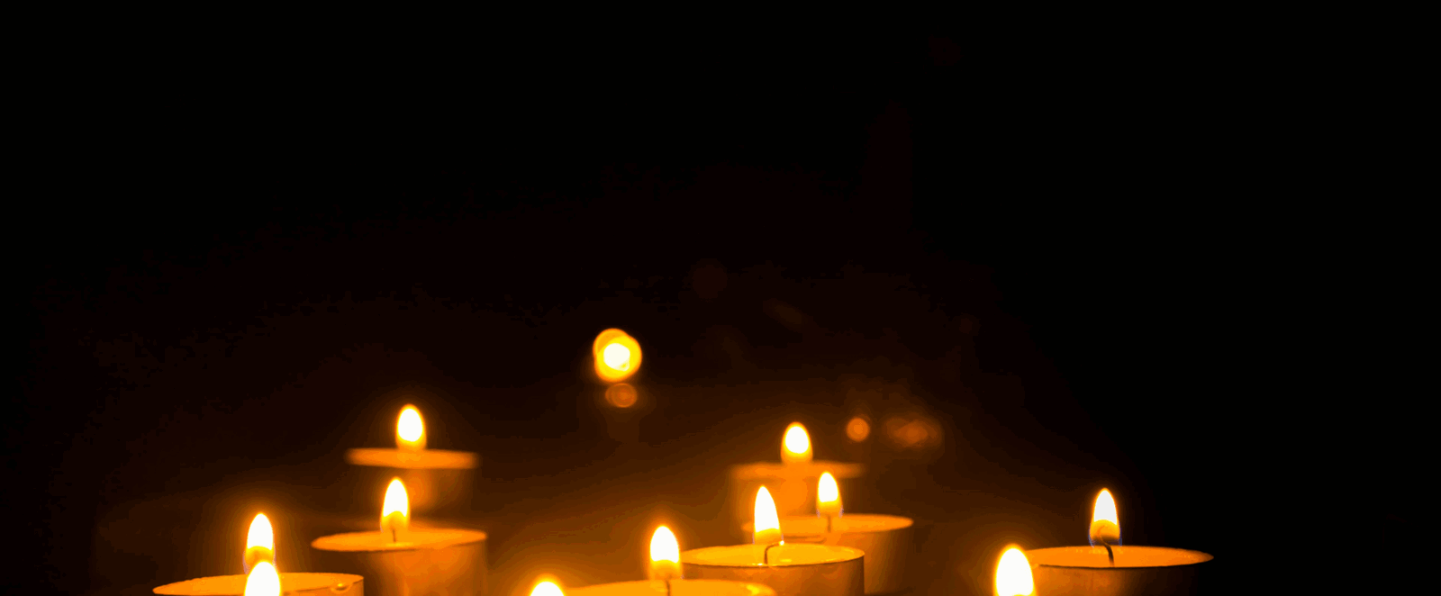 Vor einem schwarzen Hintergrund brennen Teelichter. 