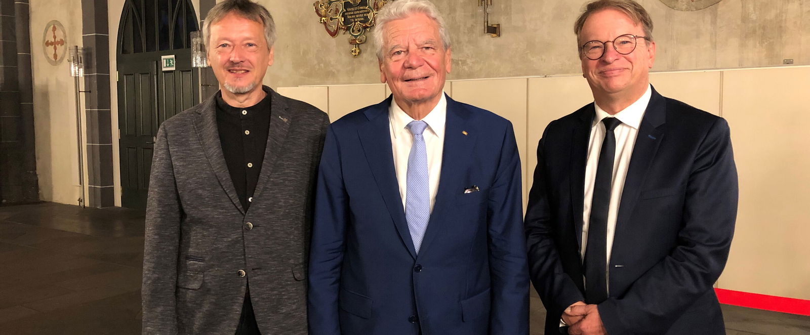 Drei Männer in Anzügen schauen in die Kamera.