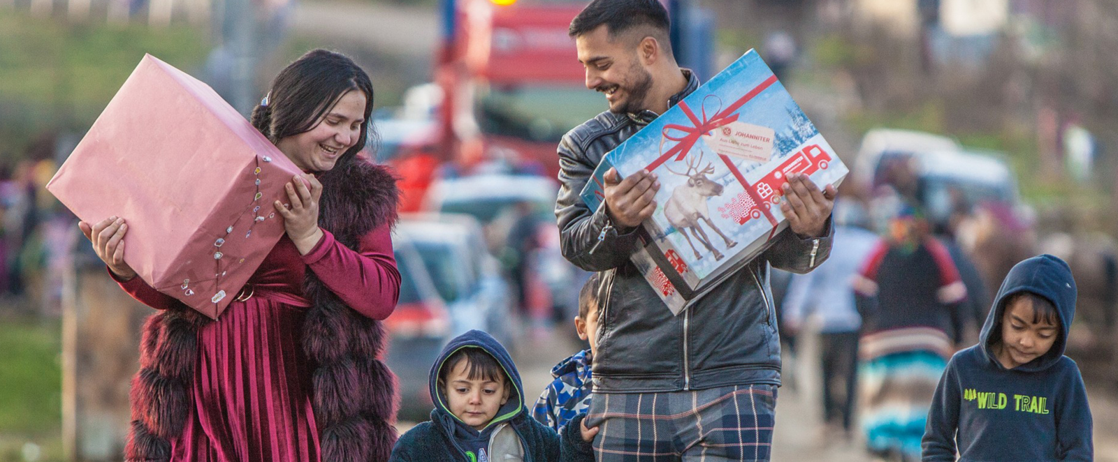 Zwei Erwachsene und zwei Kinder laufen, jeder ein Paket halten, eine Straße entlang.