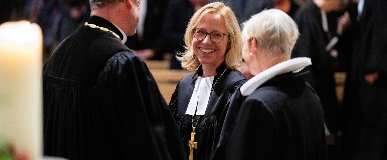 In junge Bischöfin lächelt einem Kollegen und einer Kollegin zu.