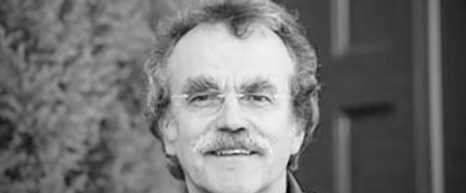 Ein schwarz-weiß Bild eines Mannes mit Schnauzbart und Brille.