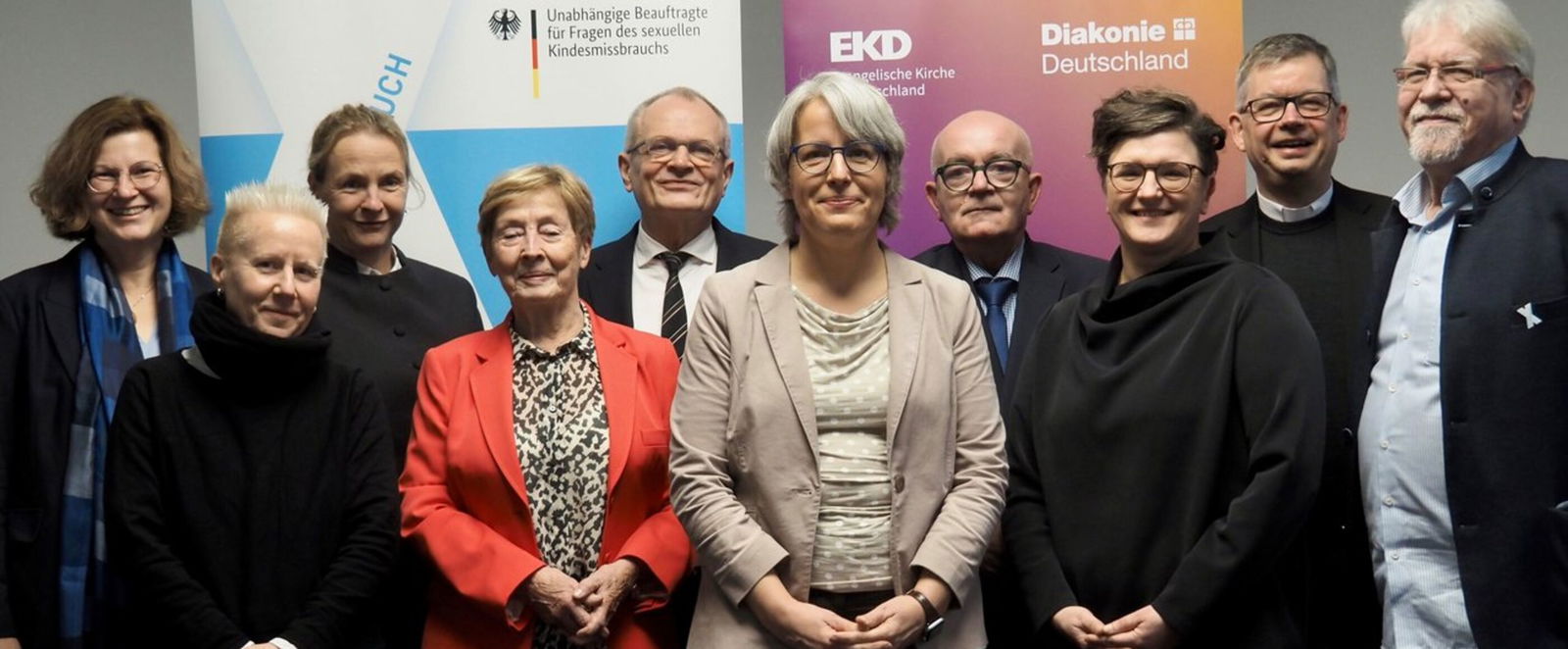 Mehrere Frauen und Männer haben sich vor Aufstellern der Bundesregierung, der EKD und der Diakonie zum Gruppenbild aufgestellt.