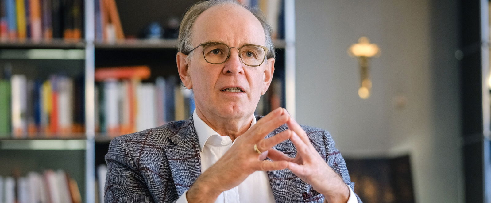 Ein mittelalter Mann mit hoher Stirn sitzt vor einer Bücherwand