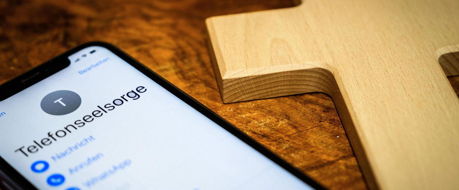 Neben einem Kreuz liegt ein Mobiltelefon, auf dem Telefonseelsorge zu lesen ist.