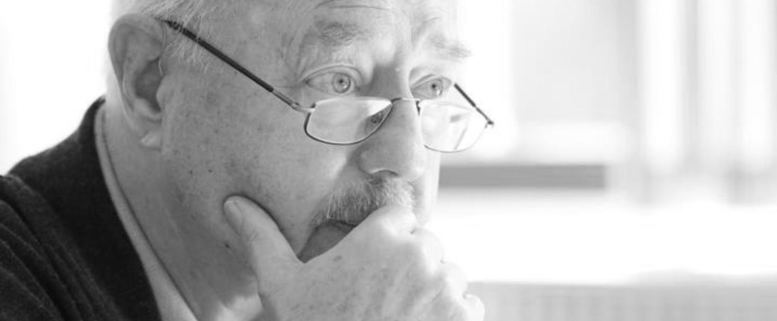 Ein schwarzweißes Bild von einem Mann mit schmaler Brille. Er stützt sich nachdenklich auf eine Hand. 