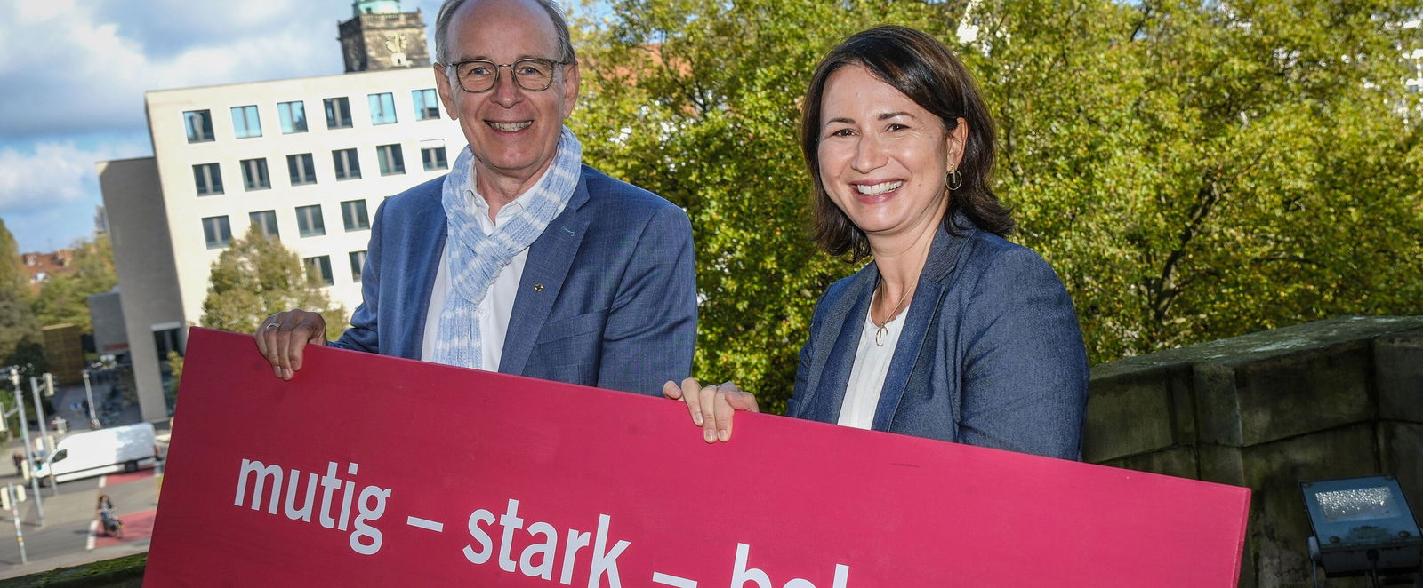 Ein Mann und eine Frau halten ein Banner mit der Aufschrift „mutig - stark – beherzt“.