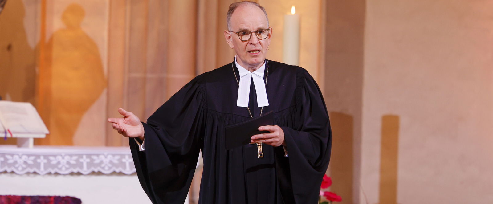Ein Bischof im schwarzen Talar predigt in einer Kirche.