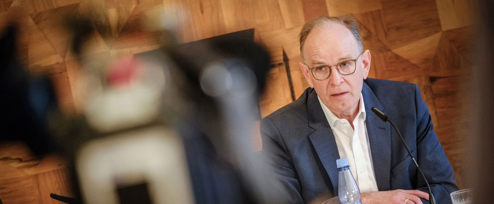 Ein Mann mit hoher Stirn und Brille sitzt vor einem Mikrofon.