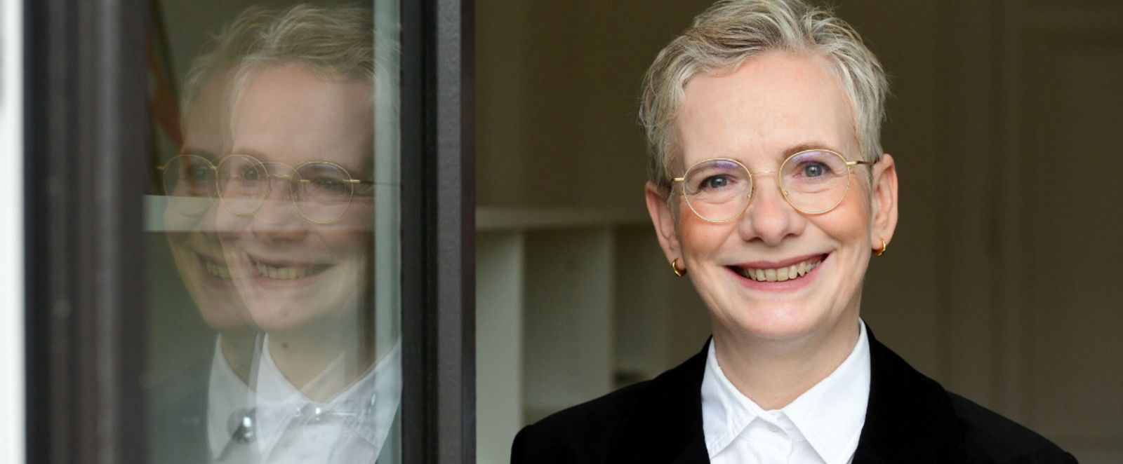 eine Frau lehnt sich an einer Glastür an. Links spiegelt sich ihr Kopf in der Tür.