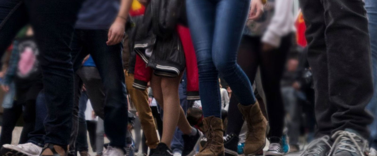 Blick aus der Froschperspektive auf eine Straße, auf der viele Menschen laufen, man sieht nur Schuhe und Beine.