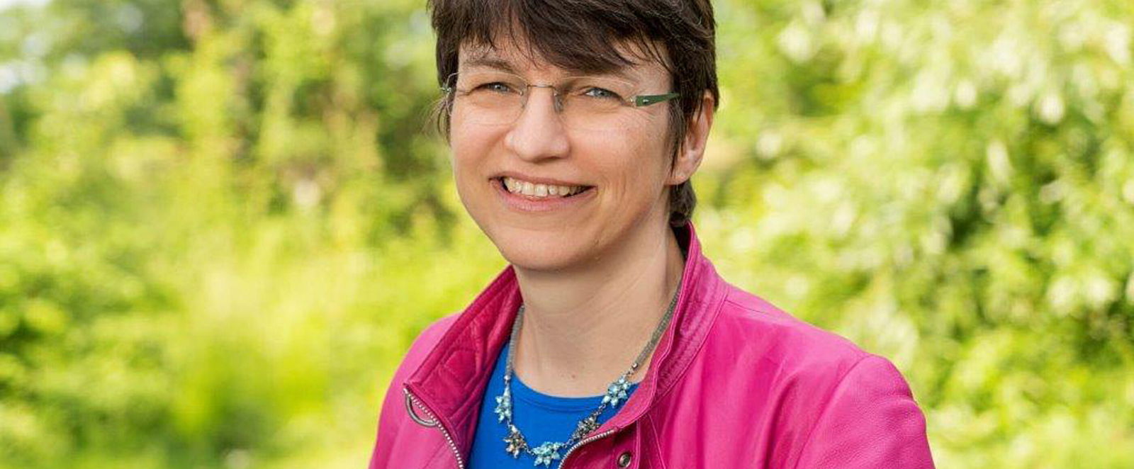 Eine als Frau lesbare Person steht im Grünen.