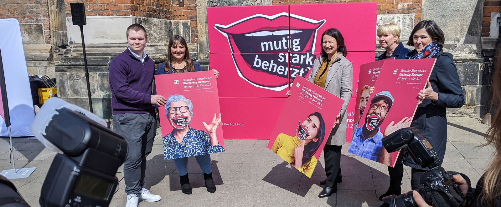 Eine Gruppe von Menschen präsentiert ein Plakatmotiv mit einem lächelnden Mund.