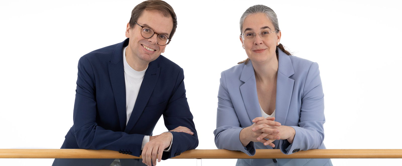 Eine als Mann und eine als Frau lesbare Person lehnen an einem Geländer.