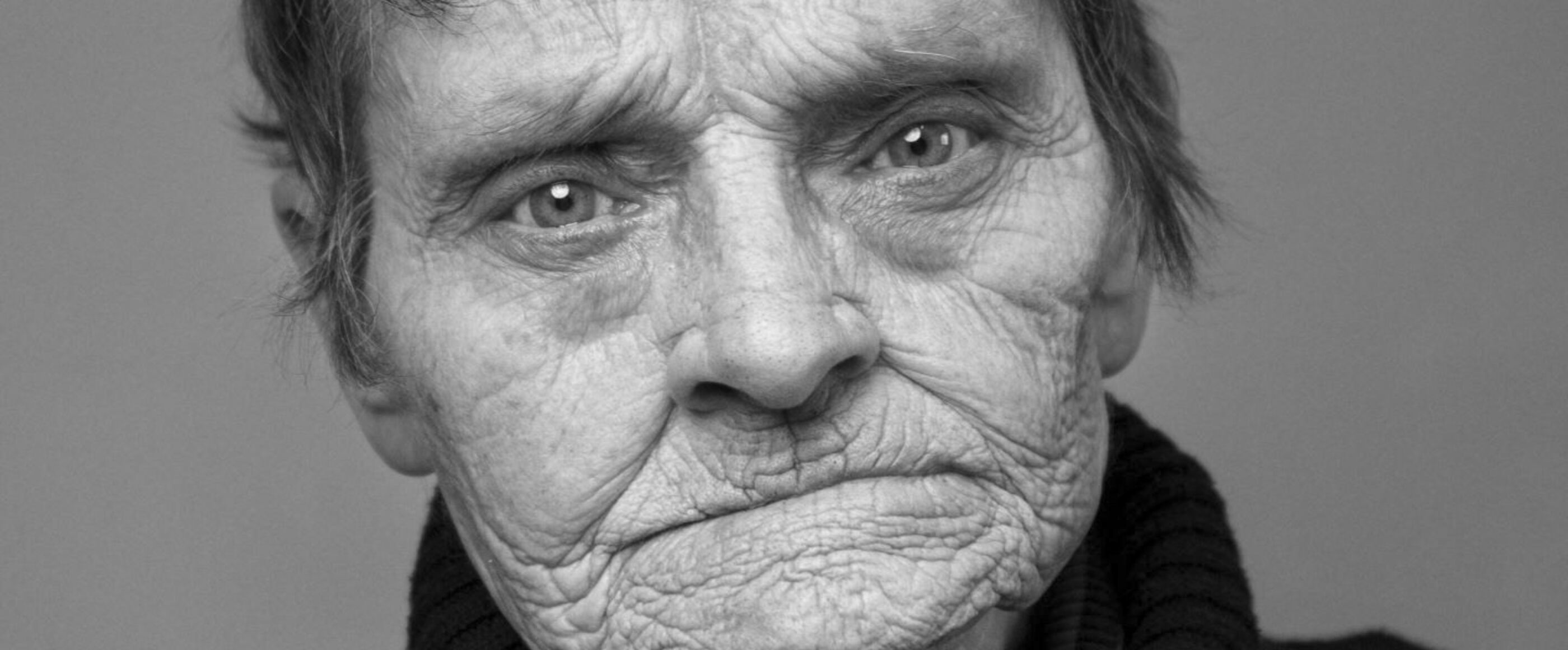 Eine Schwarzweißfotografie von einer als Frau lesbaren Person mit kurzen Haaren und faltiger Haut.