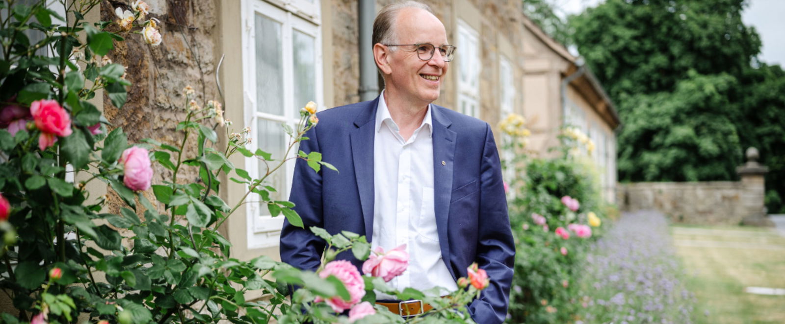 Eine männlich gelesene Person in einem Garten mit Rosen