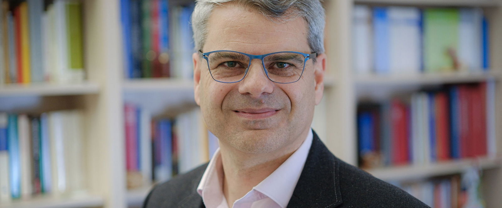 Eine als Mann lesbare Person vor einer Bücherwand.