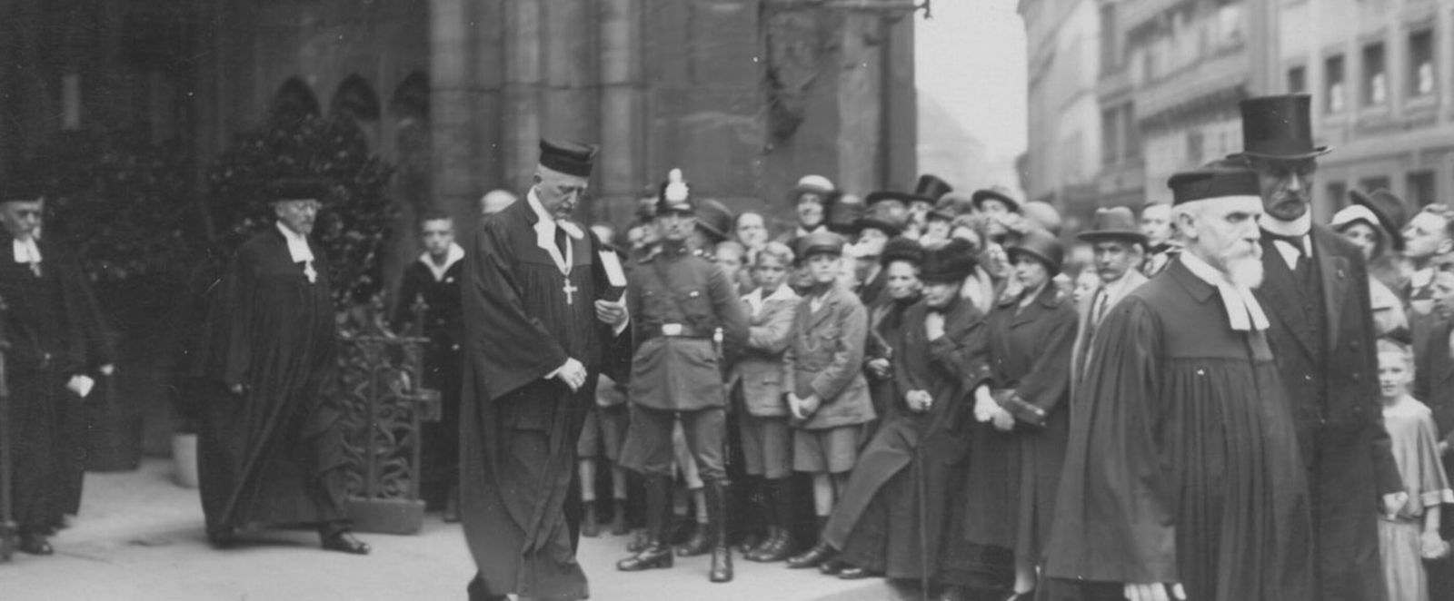 Eine historische Schwarzweiß-Aufnahme: Mehrere Männer ziehen aus einer Kirche aus.