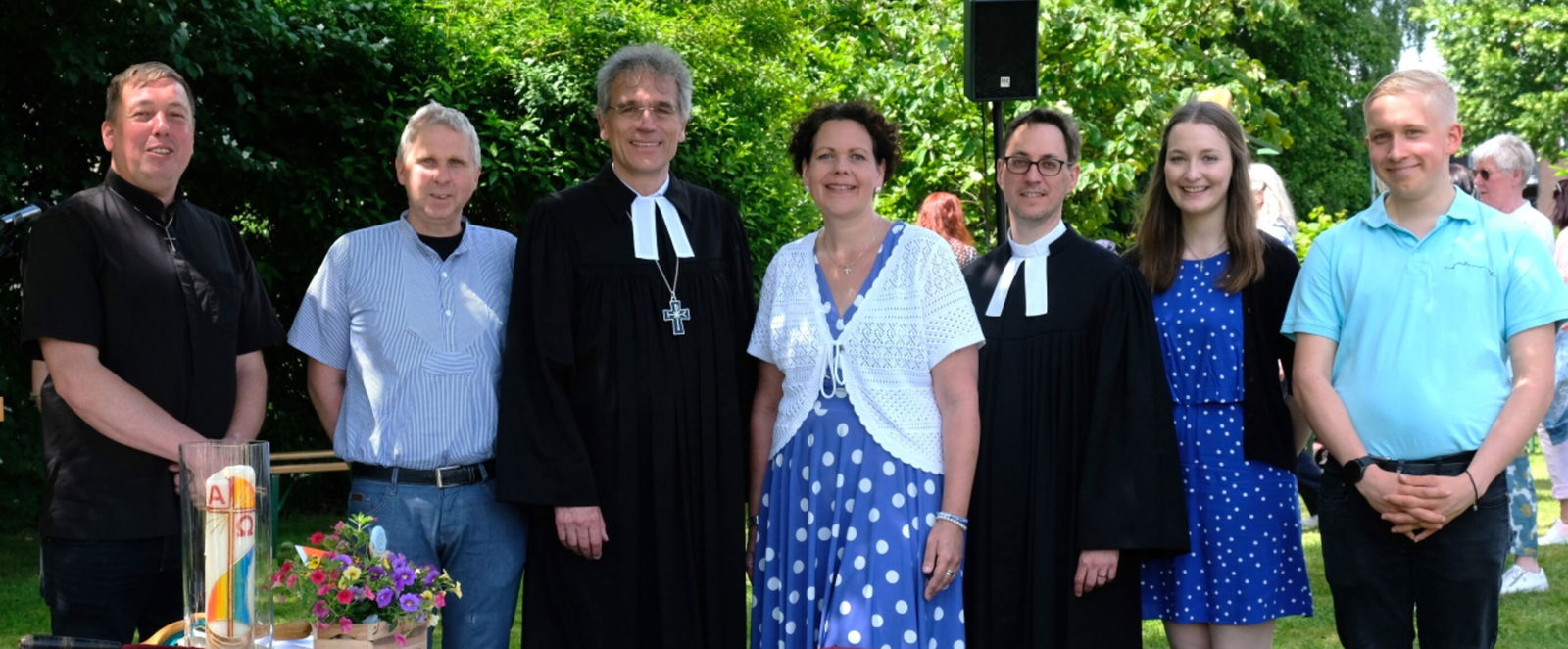 Sieben Personen, fünf männlich gelesene und zwei weiblich gelesene stehen zusammen, zwei tragen Talar.