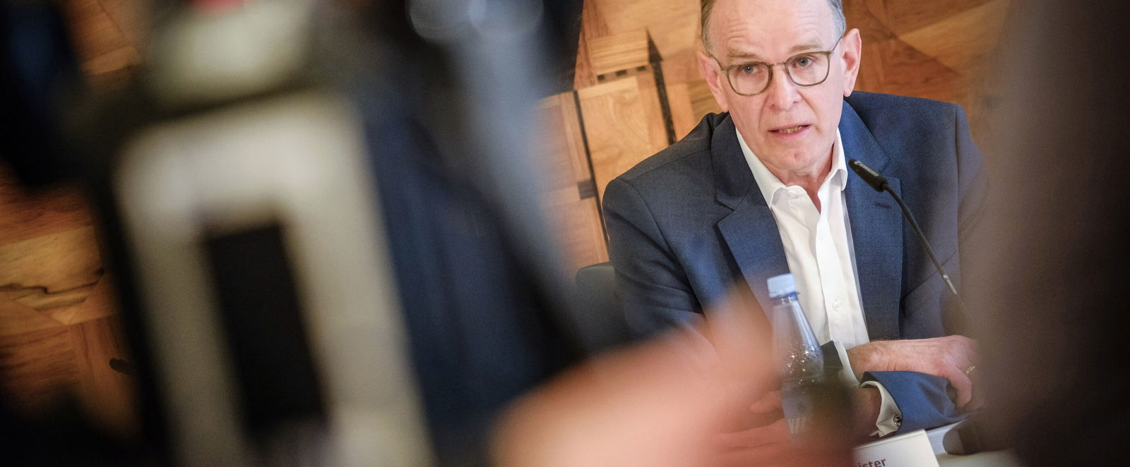 Eine als Mann lesbare Person spricht mit nachdenklichem Gesicht in Fernsehkameras.