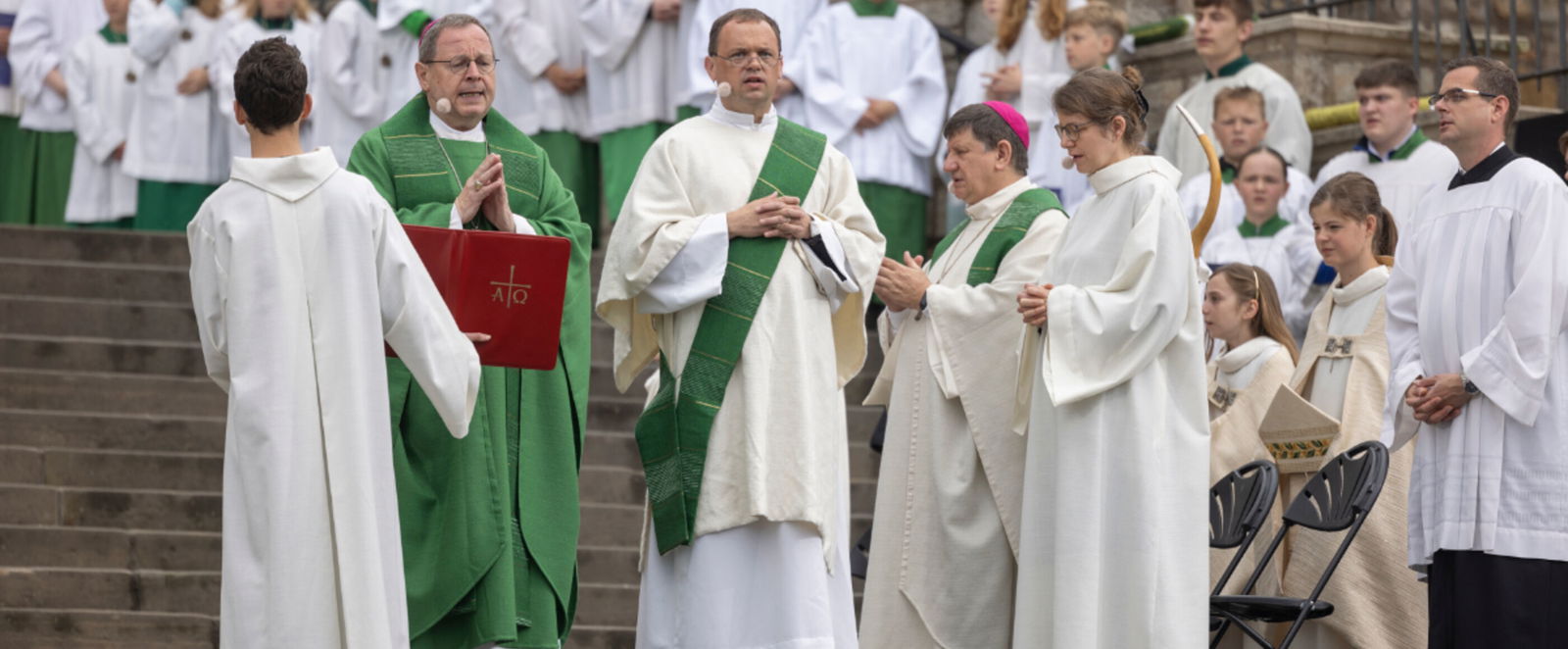 katholische Geistliche stehen auf den Stufen eines Gebäudes und predigen.