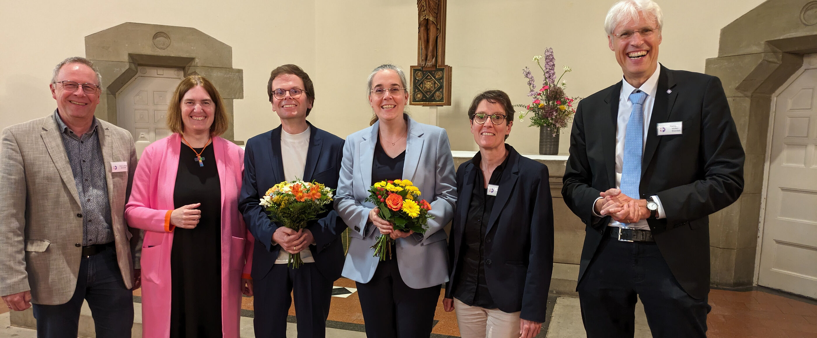Eine Gruppe aus weiblich und männlich lesbaren Personen steht vor einem Altar in einer Kirche.