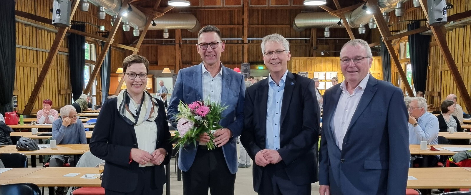 Eine als Frau lesbare Person und drei als Männer lesbare Personen stehen in einem Saal.