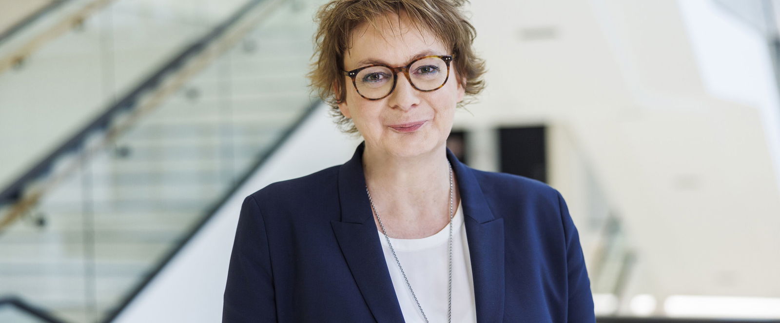 Eine als Frau lesbare Person mit Brille und kurzen Haaren