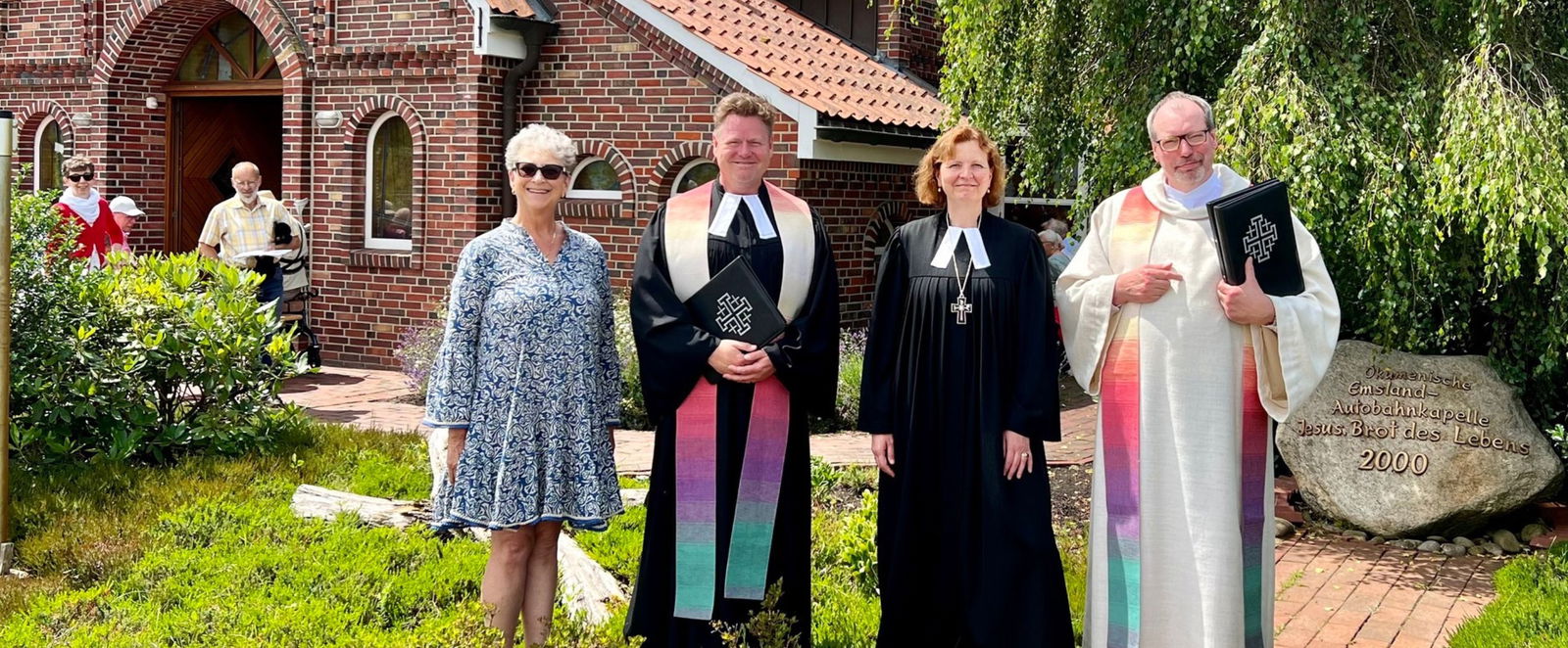 eine Gruppe von Menschen vor einer Autobahnkirche aus Backstein an einem Sommertag