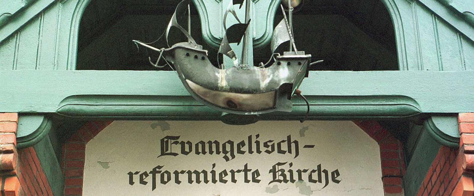 Der Eingang einer Kirche. Über der Tür ein Schiff aus Stahl.