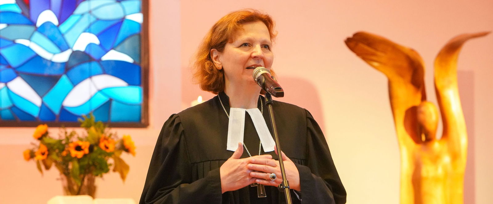 Eine Frau im Talar steht vor einem blauem Buntglasfenster und einer goldenen Skulptur: Regionalbischöfin Sabine Schiermeyer