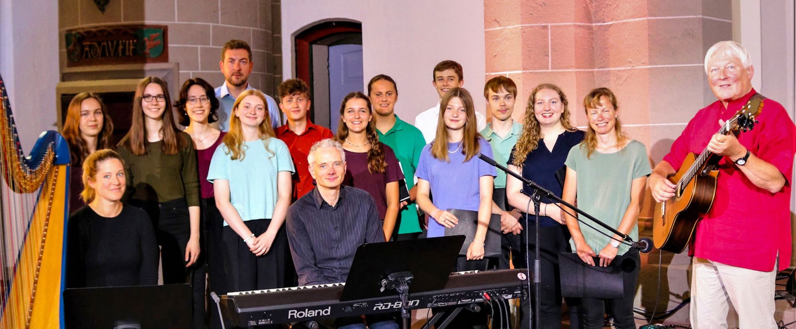 Mehrere Menschen stehen neben einer Harfe. Eine männlich gelesene Person steht rechts mit einer Gitarre.
