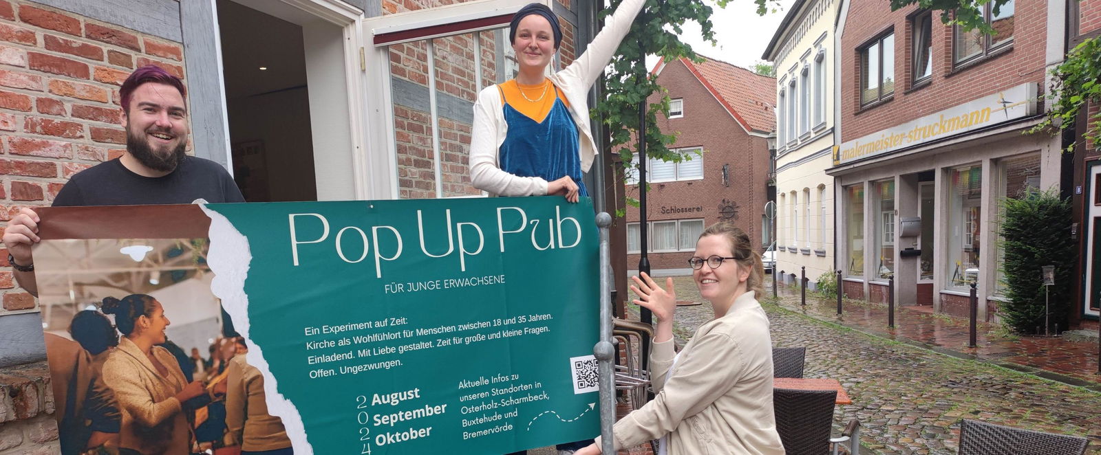 Drei junge Menschen lächeln und halten ein grünes Schild, auf dem Pop Up-Pub steht hoch.