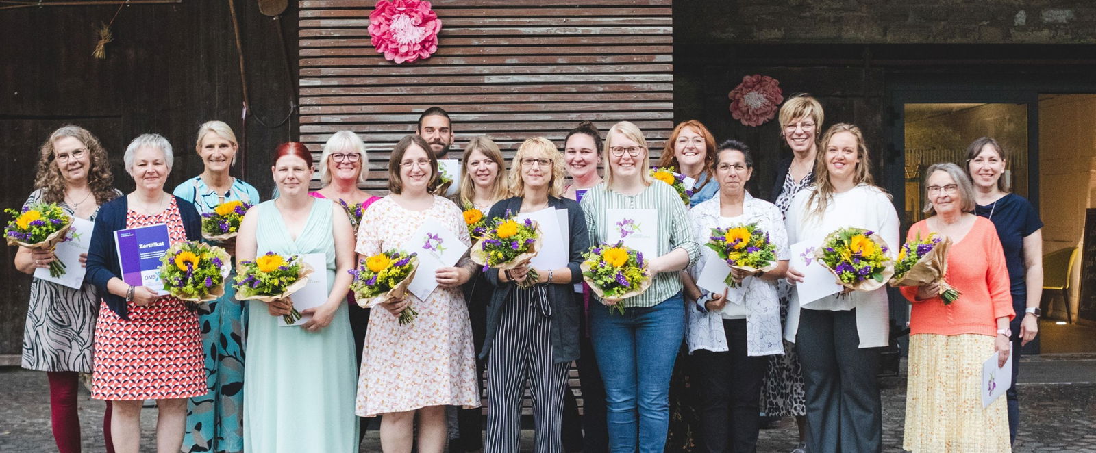 eine Gruppe von Menschen mit Blumensträußen in der Hand vor einem Gebäude