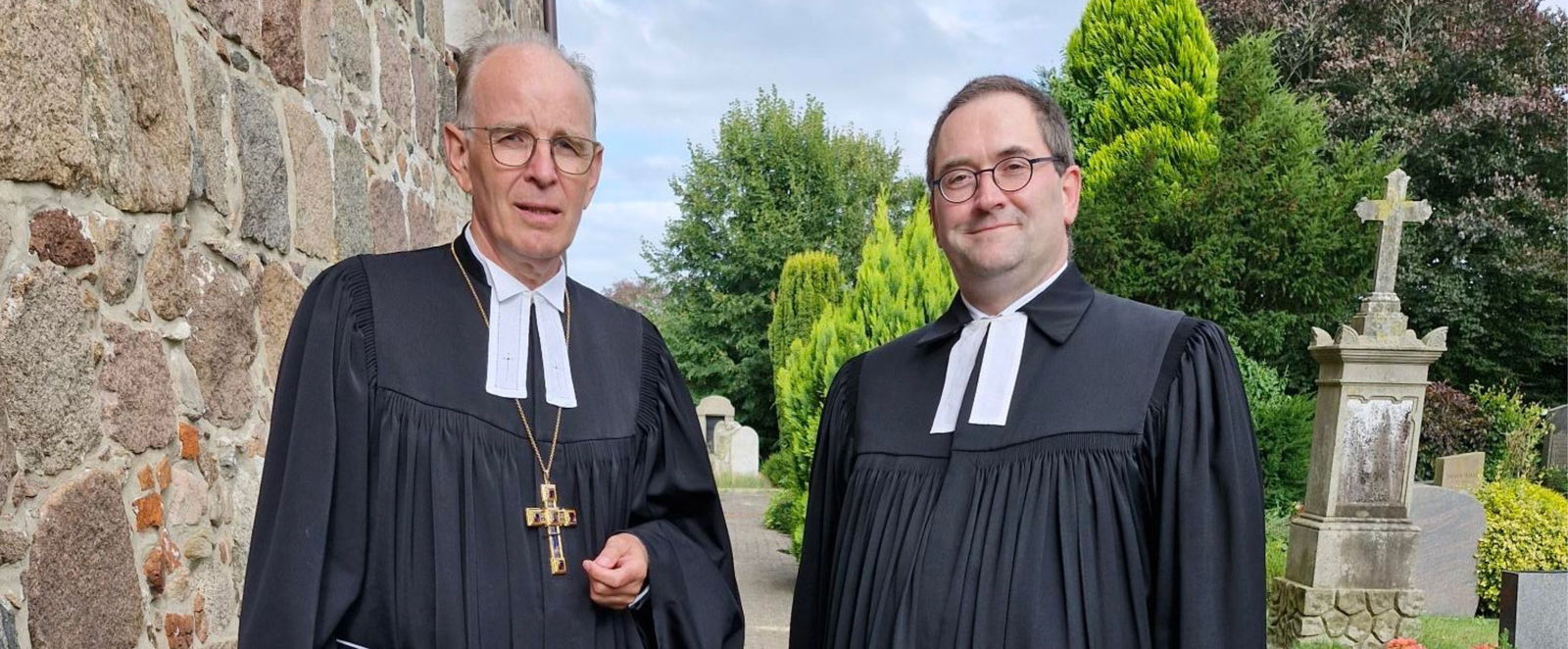 zwei Männer in Talaren vor einer Kirche
