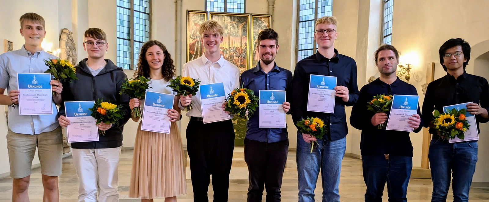Eine Gruppe junger Menschen lächeln und halten Urkunden und Sonnenblumen.