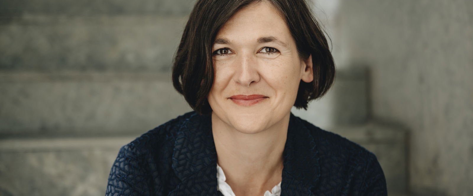 Portraitfoto einer als Frau lesbaren Personen mit schulterlangen dunklen Haaren.