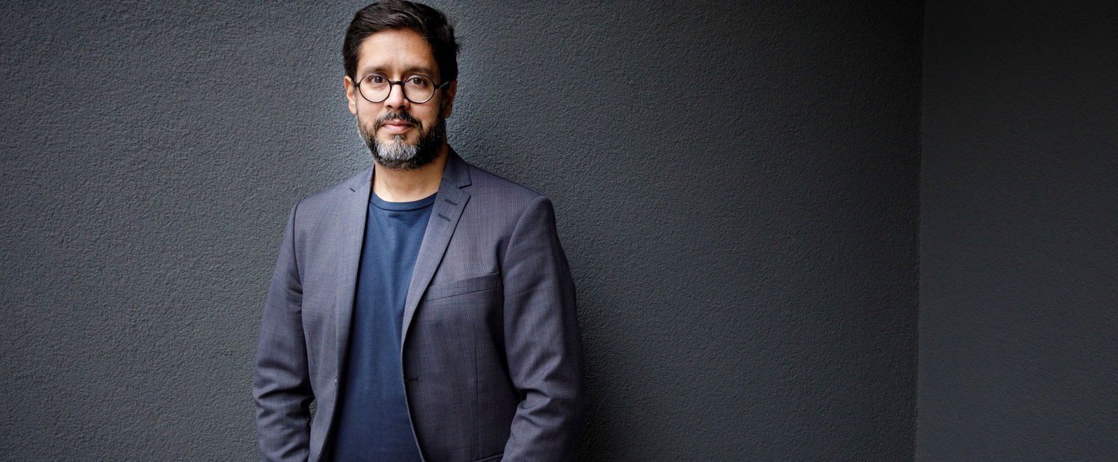 ein Mann vor einem dunklen Hintergrund schaut freundlich in die Kamera.