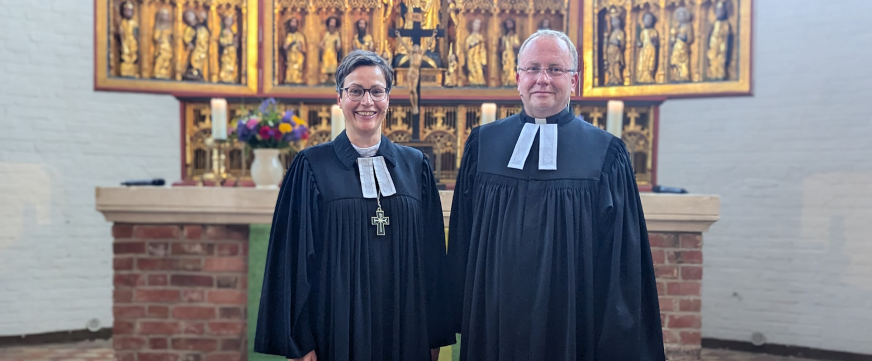 Zwei Personen in Talaren stehen in einer Kirche.