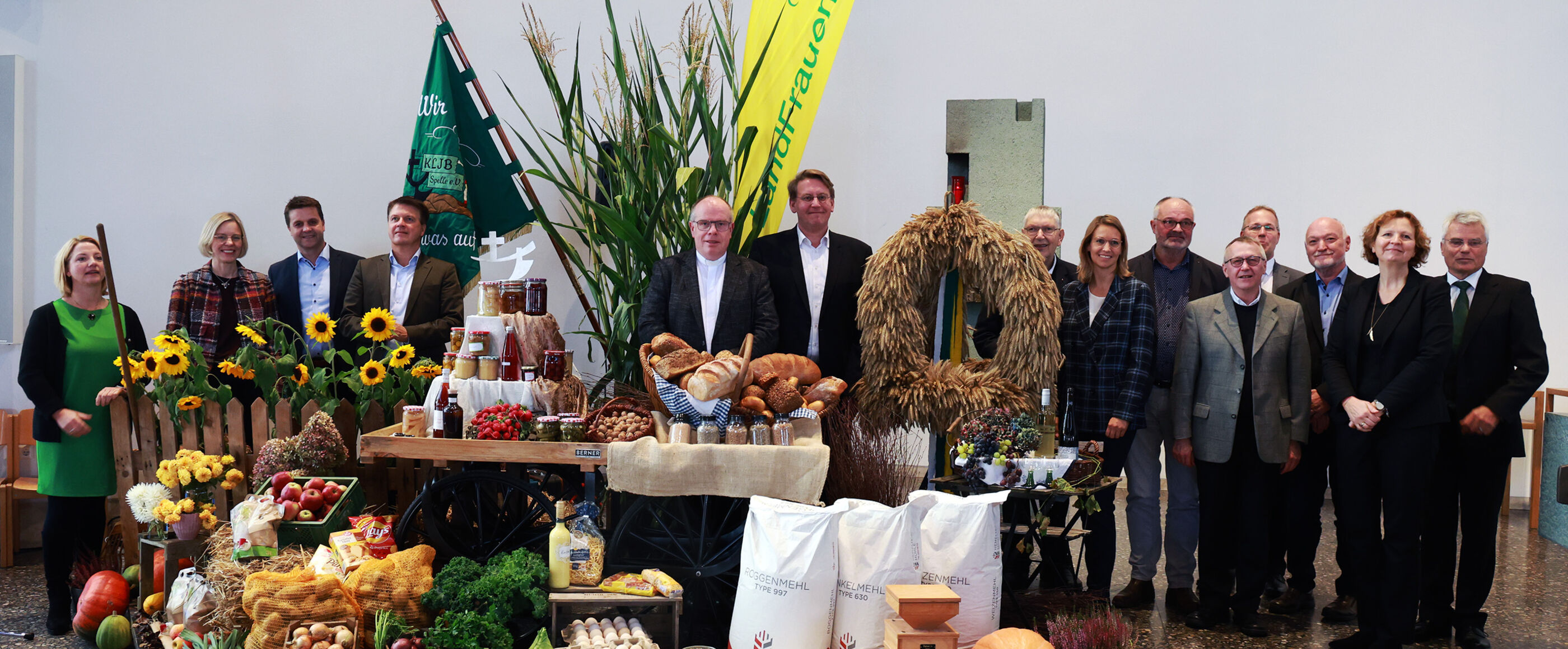 Neben einem Gabentisch voller Feldfrüchte stehen mehrere Menschen.