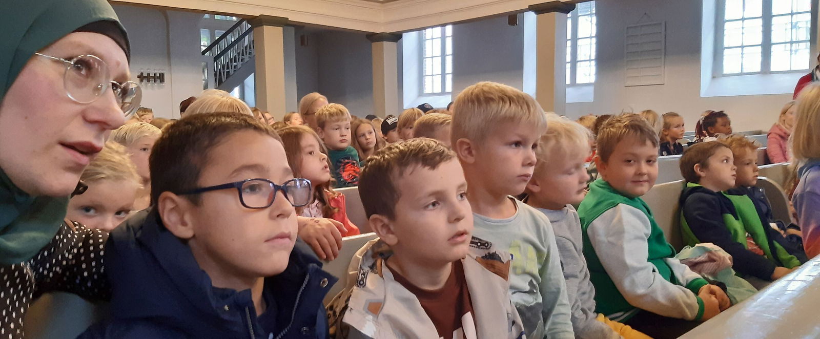 Mehrere Kinder sitzen in Kirchenbänken und schauen gebannt nach vorn.