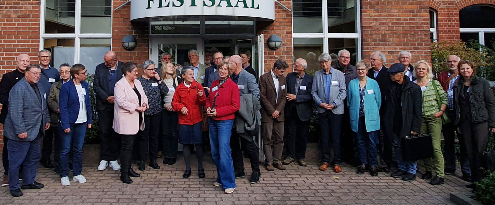 Eine Gruppe steht vor einem Gebäude mit dem Schild Festsaal.