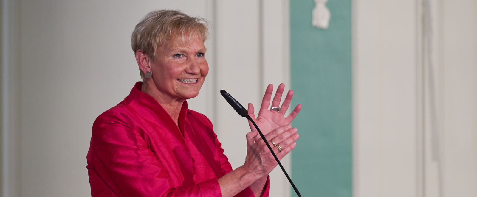 Eine weiblich gelesene Person in rotem Jackett steht vor einem Mikro an einem Redepult auf dem steht "EKD".