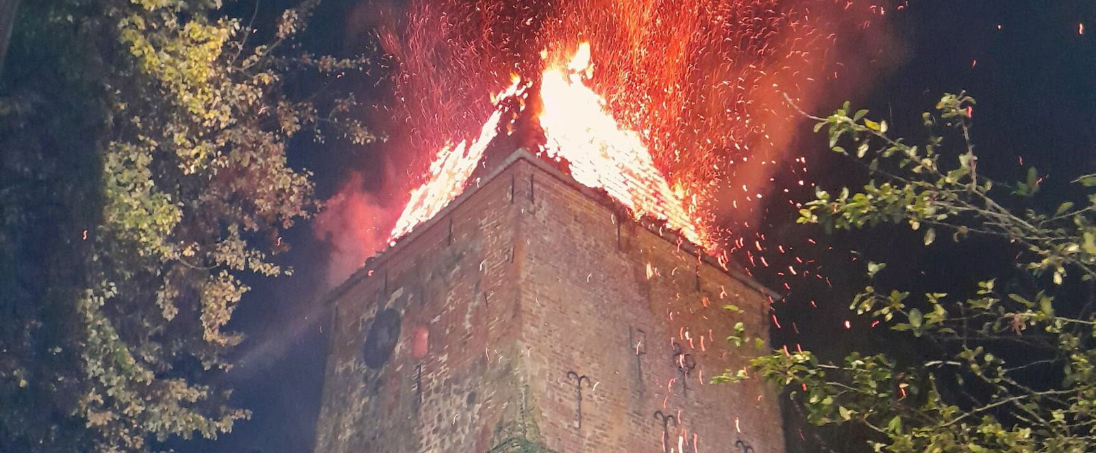 Ein Kirchturm brennt. Die Kirchturmspitze steht in Flammen